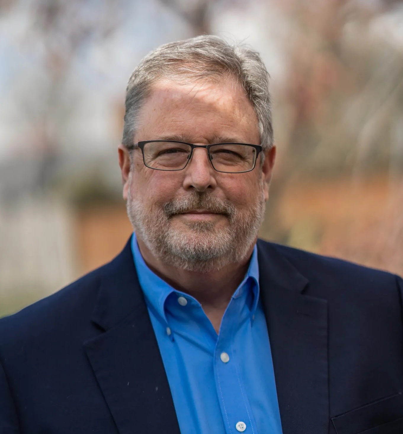 Headshot of Vance looking into the camera wearing a blue dress shirt, glasses, and a navy suit coat.