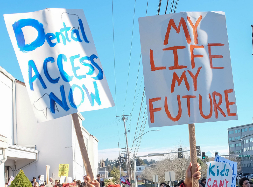 Photo of protest signs saying, "Dental Access Now and My Life My Future" 